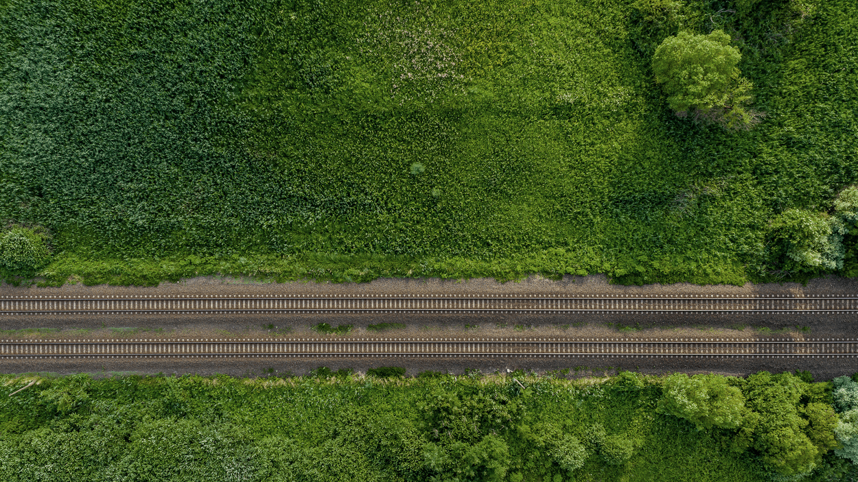Flybilde av jernbaneskinner og grønne marker.